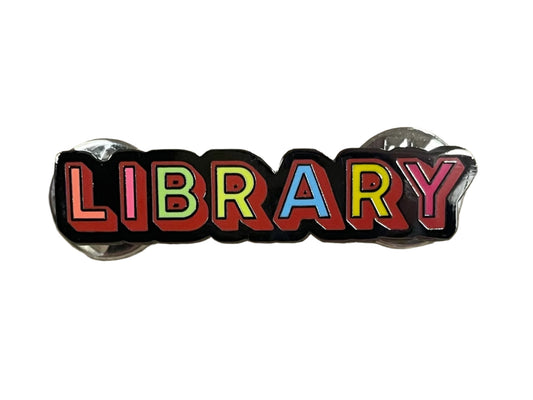 front of enamel pin that says library in rainbow letters on a black background