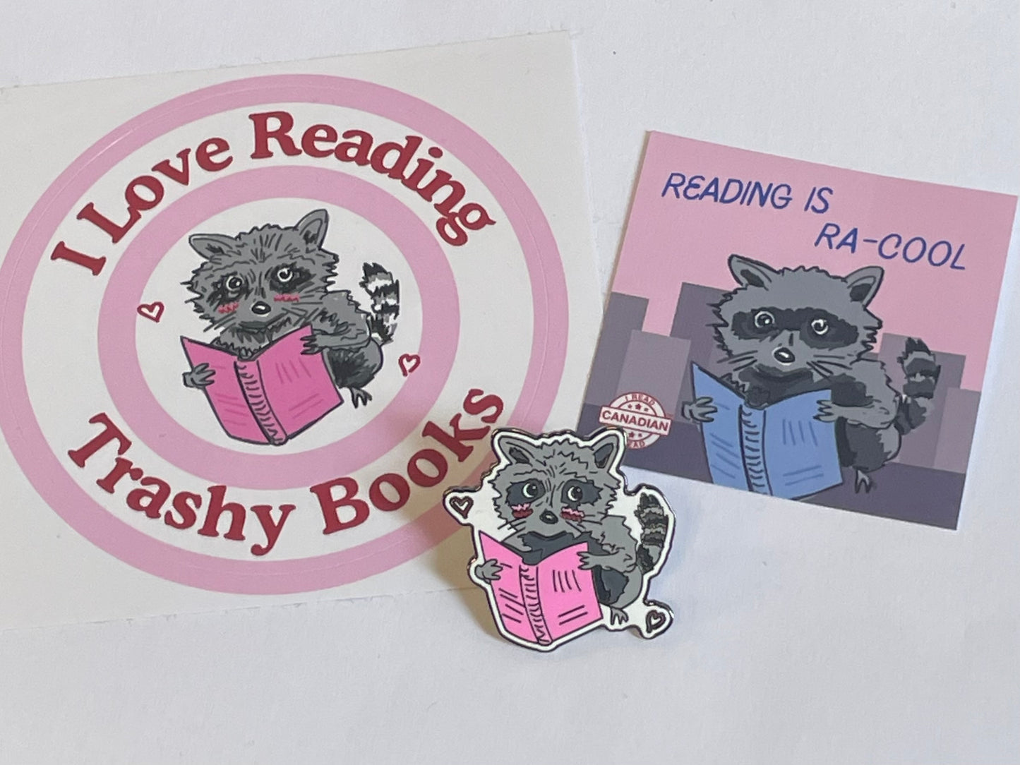 raccoon pin in front of the i love reading trashy books sticker and the reading is ra-cool sticker