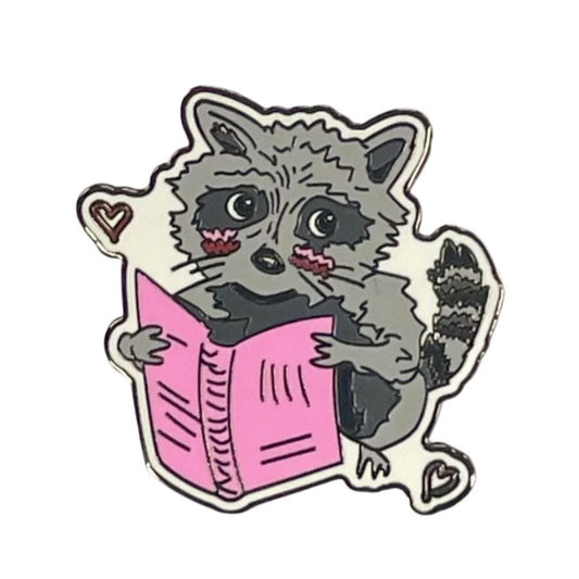front of the raccoon pin, featuring a blushing raccoon holding a book